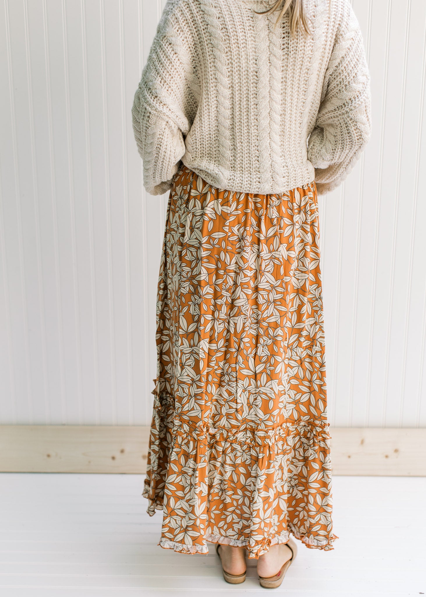 Back view of Model wearing a rust colored maxi skirt with a cream leaf pattern and an elastic waist.