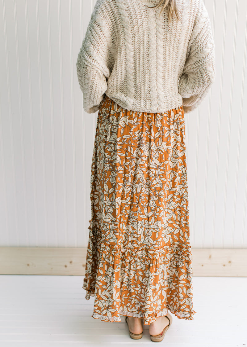 Back view of Model wearing a rust colored maxi skirt with a cream leaf pattern and an elastic waist.