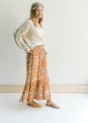 Model wearing mules with a cream sweater and a rust colored maxi skirt with a cream leaf pattern.