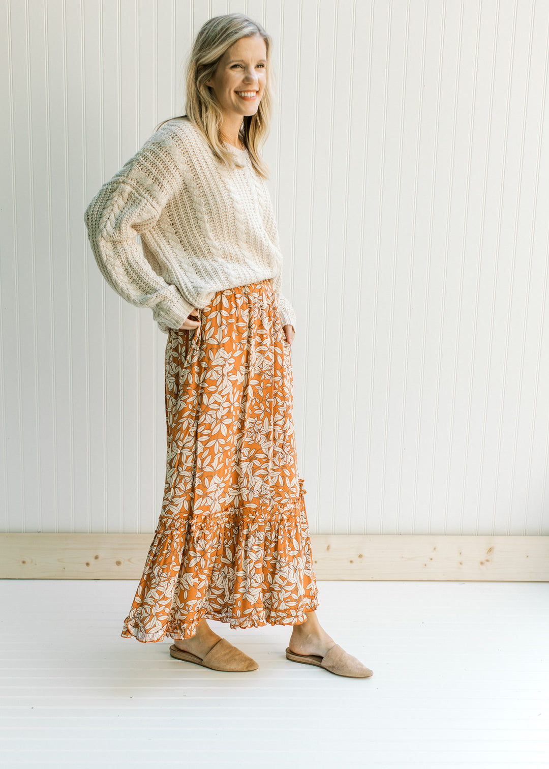 Model wearing mules with a cream sweater and a rust colored maxi skirt with a cream leaf pattern.