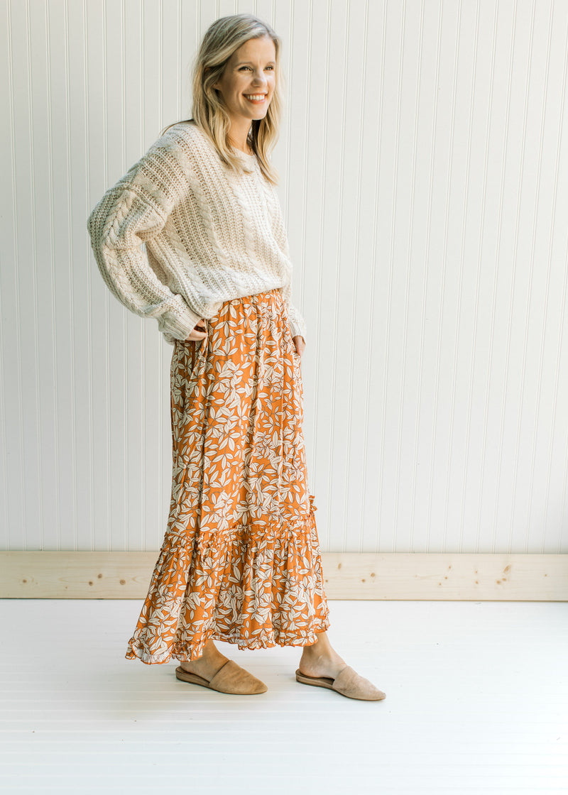 Model wearing mules with a cream sweater and a rust colored maxi skirt with a cream leaf pattern.