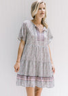 Model wearing an above the knee v-neck dress with a tie and a pink, sage and cream design. 