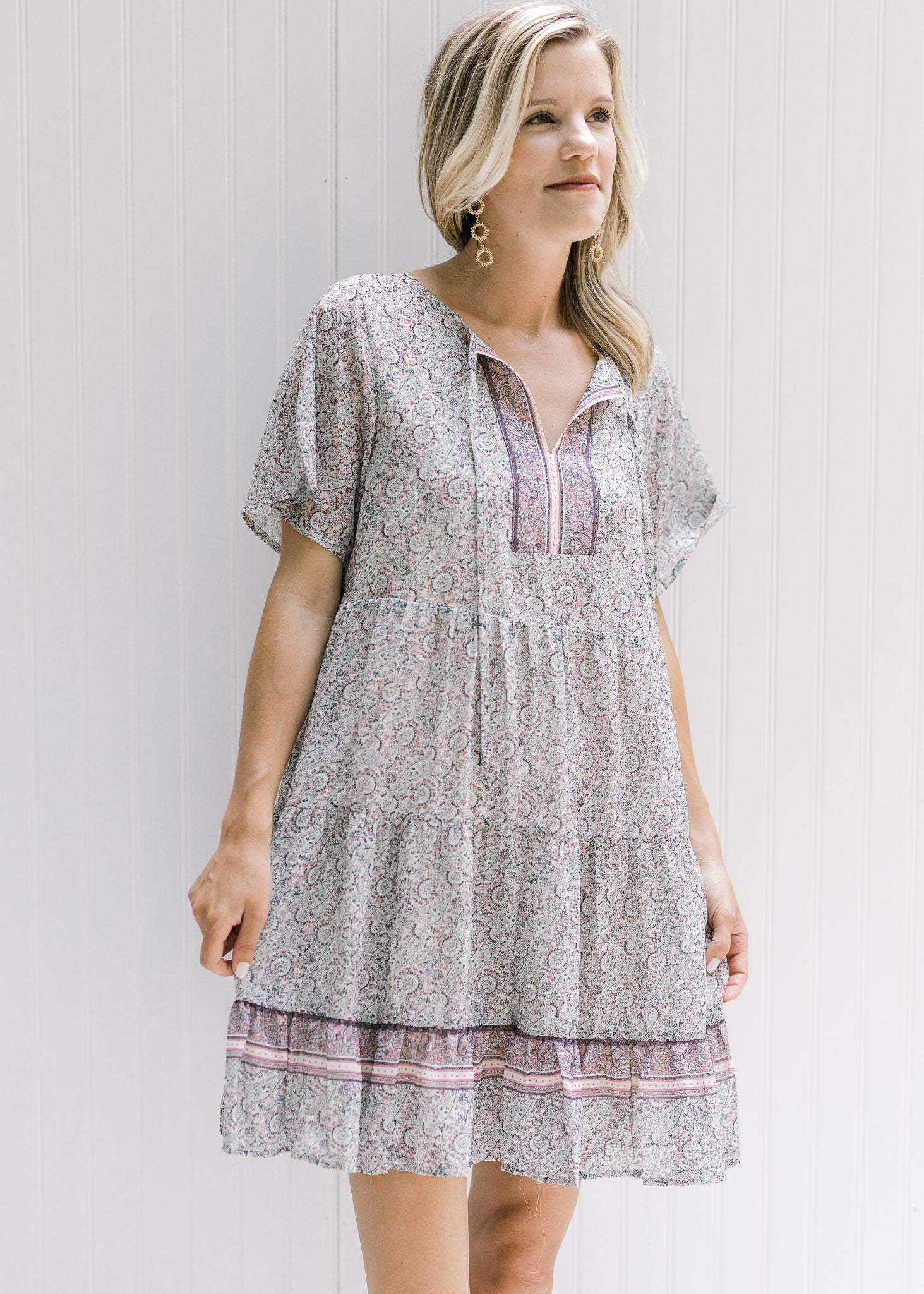 Model wearing an above the knee v-neck dress with a tie and a pink, sage and cream design. 