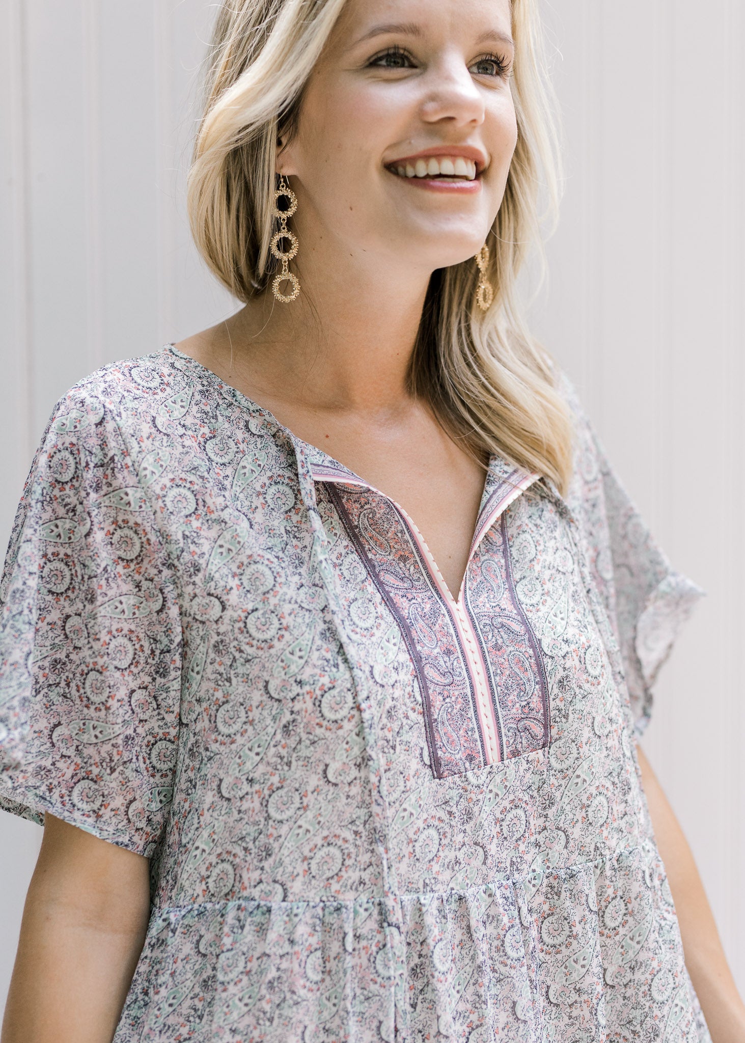 Close up view of tie on v-neck of pink, sage and cream dress with short sleeves. 