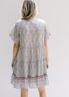 Back view of Model wearing an above the knee dress with a tie and a pink, sage and cream design. 