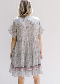 Back view of Model wearing an above the knee dress with a tie and a pink, sage and cream design. 