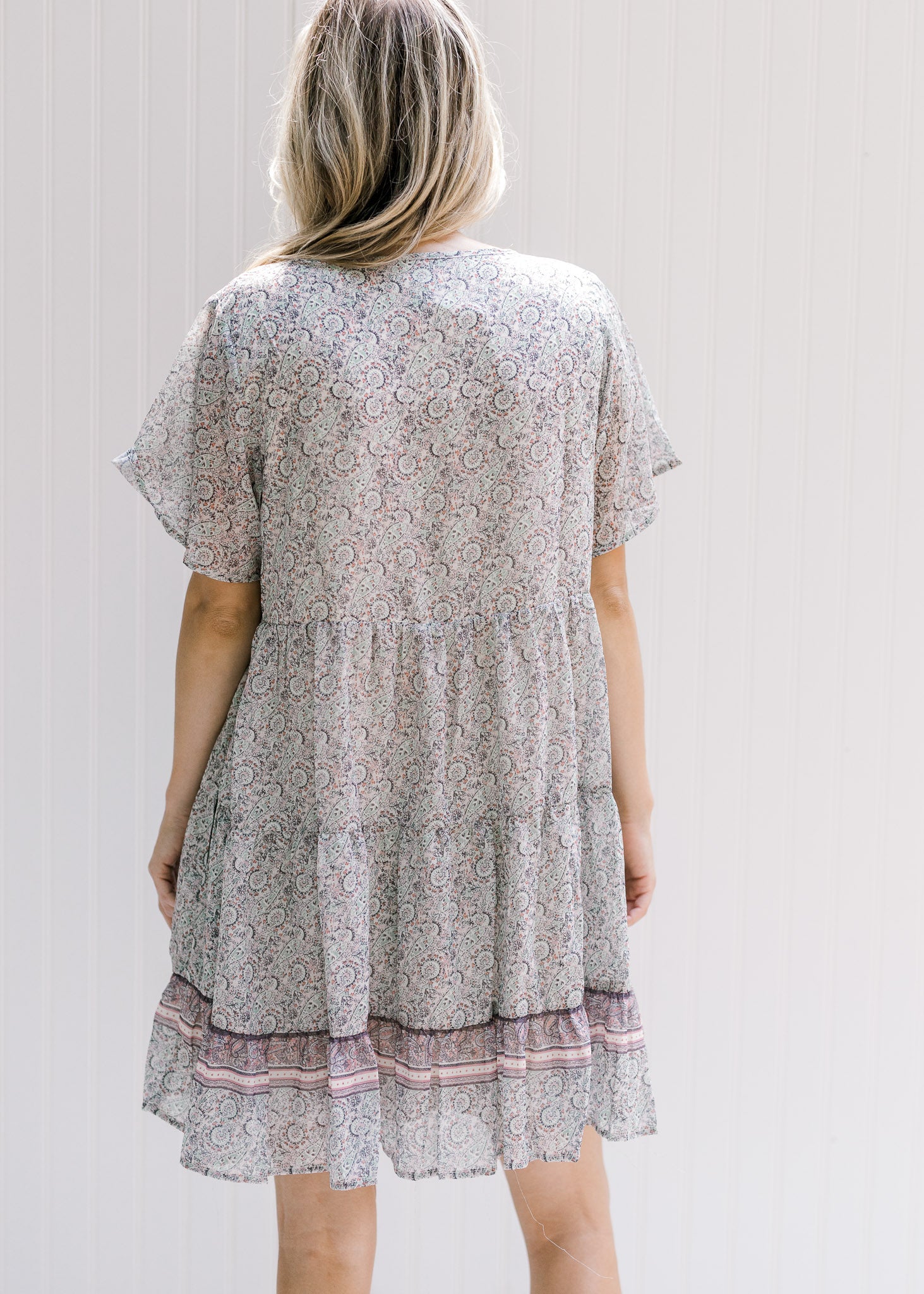Back view of Model wearing an above the knee dress with a tie and a pink, sage and cream design. 