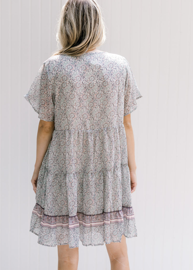 Back view of Model wearing an above the knee dress with a tie and a pink, sage and cream design. 