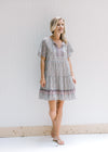 Model wearing sandals with an above the knee dress with a tie and a pink, sage and cream design. 