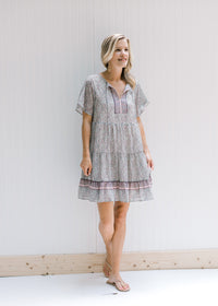 Model wearing sandals with an above the knee dress with a tie and a pink, sage and cream design. 