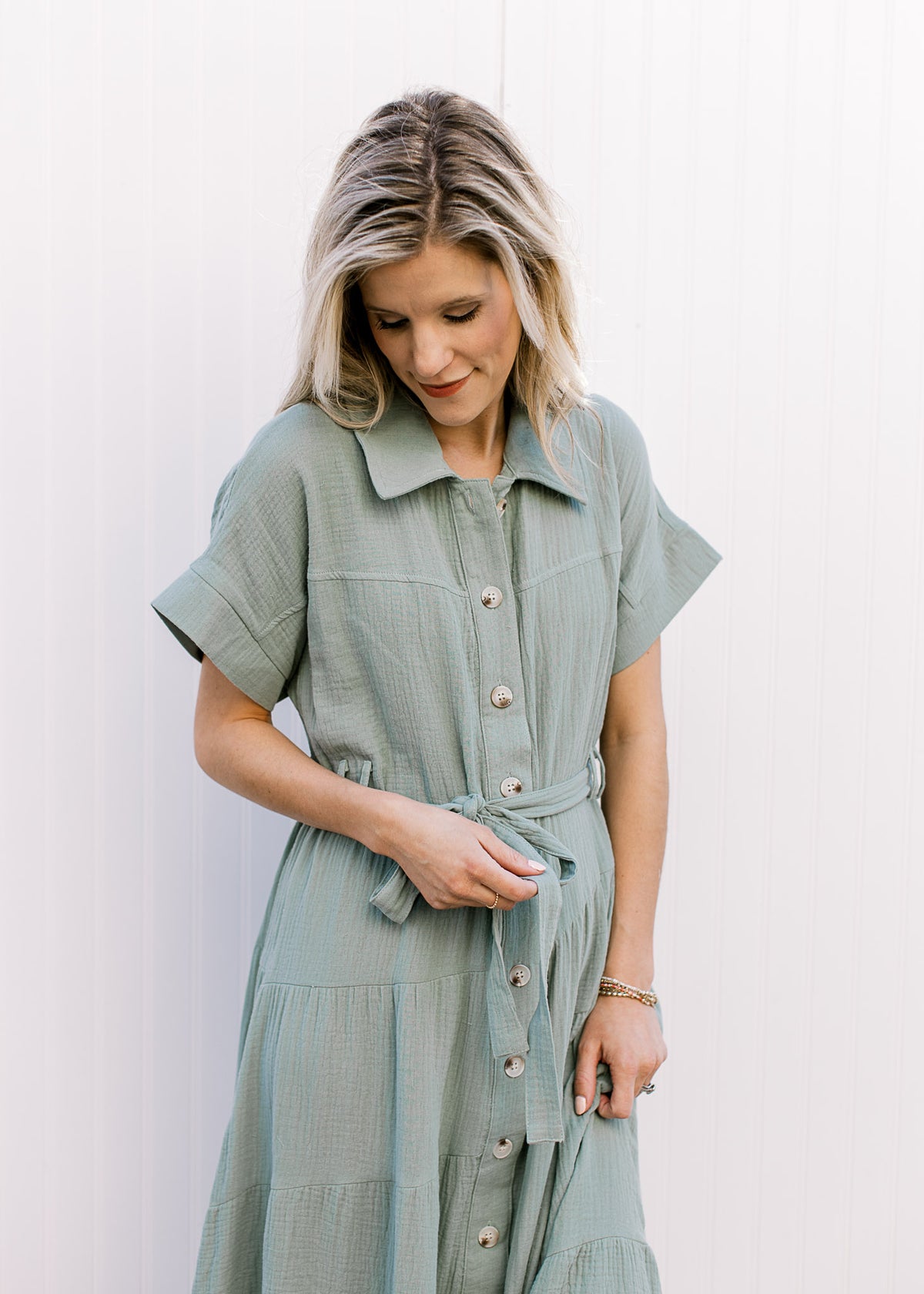 Close up of collar, short sleeves and tie belt on a gauze sage green maxi with a button front. 