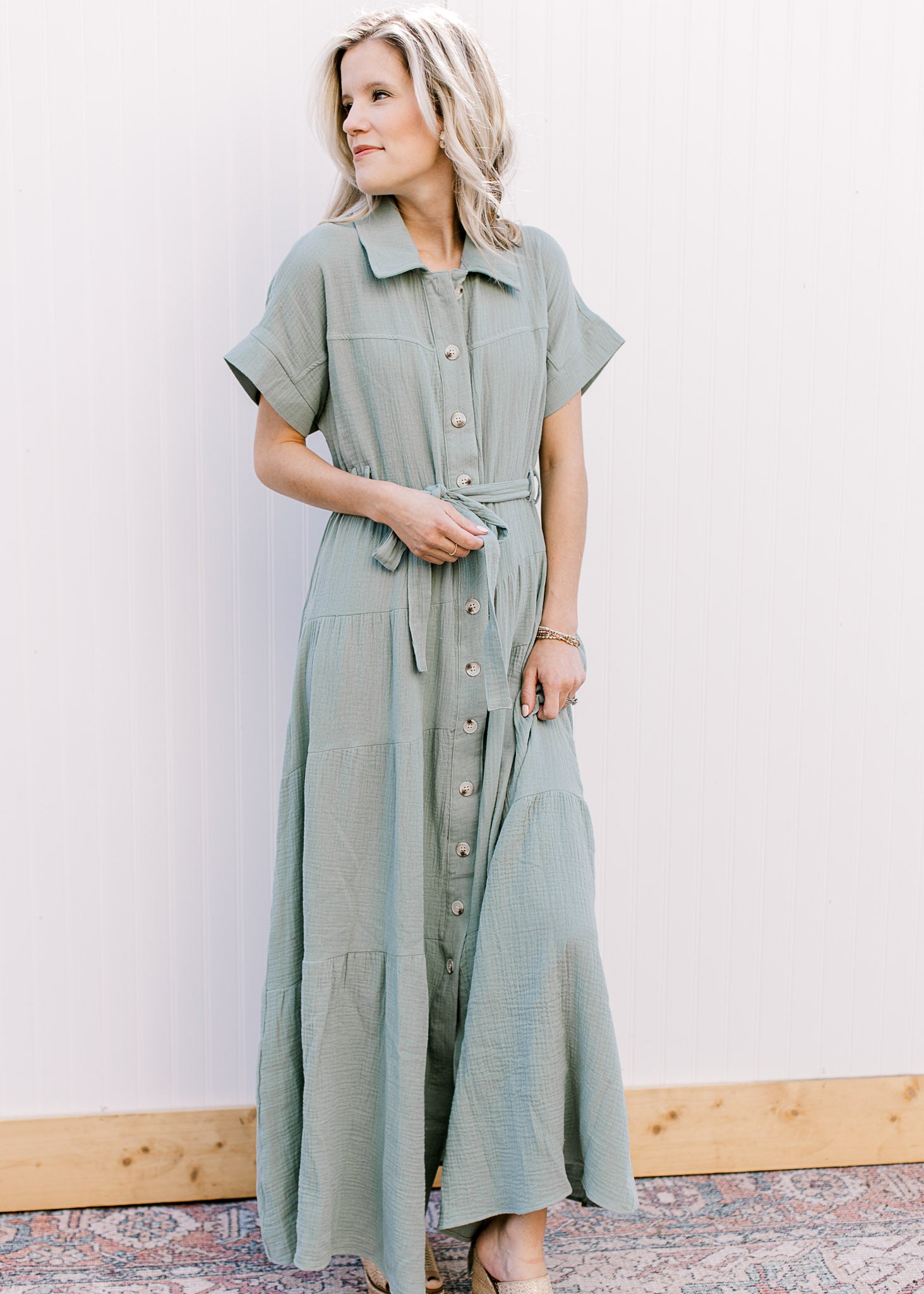 Model wearing a short sleeve sage maxi with gauze material, button front closure and a tie belt. 