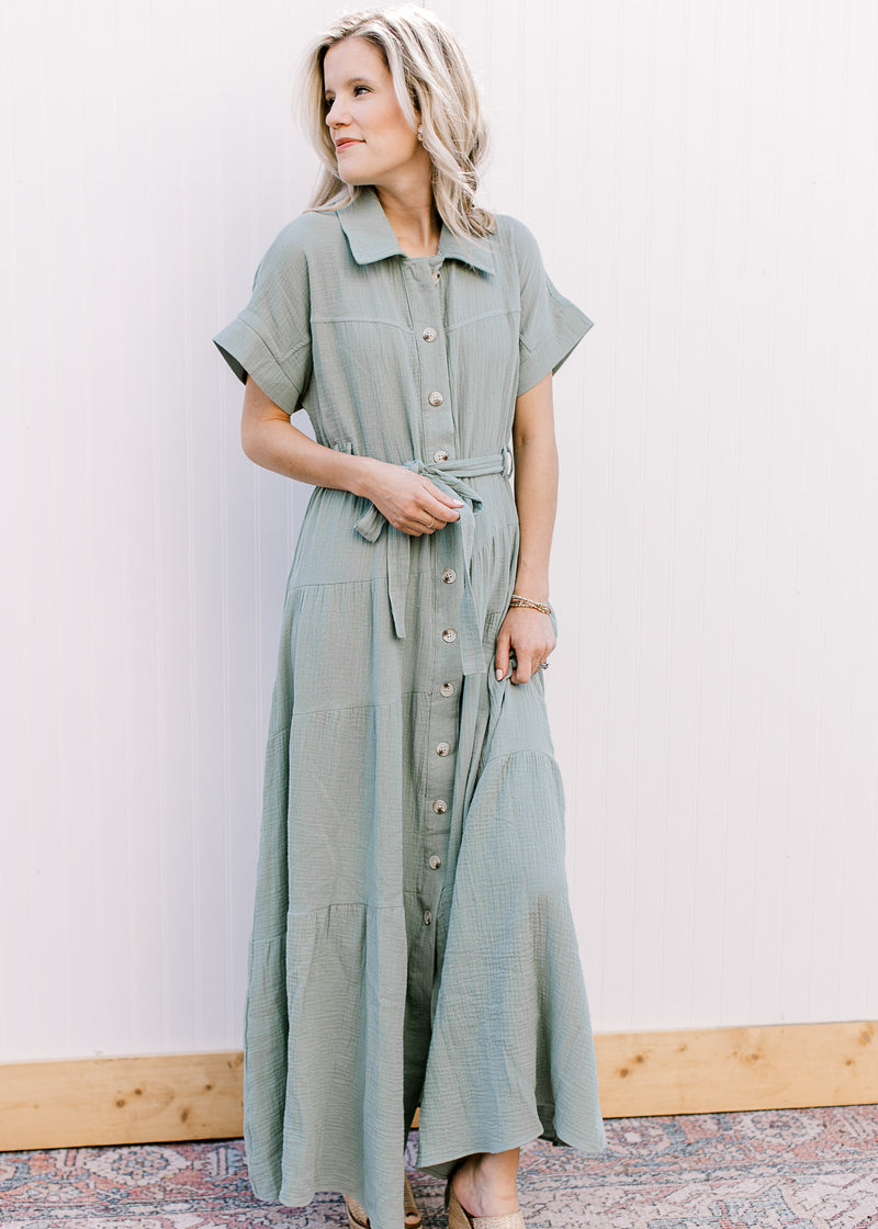 Model wearing a short sleeve sage maxi with gauze material, button front closure and a tie belt. 