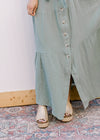 Close up of tiers along the skirt of a sage green maxi with button front and short sleeves. 