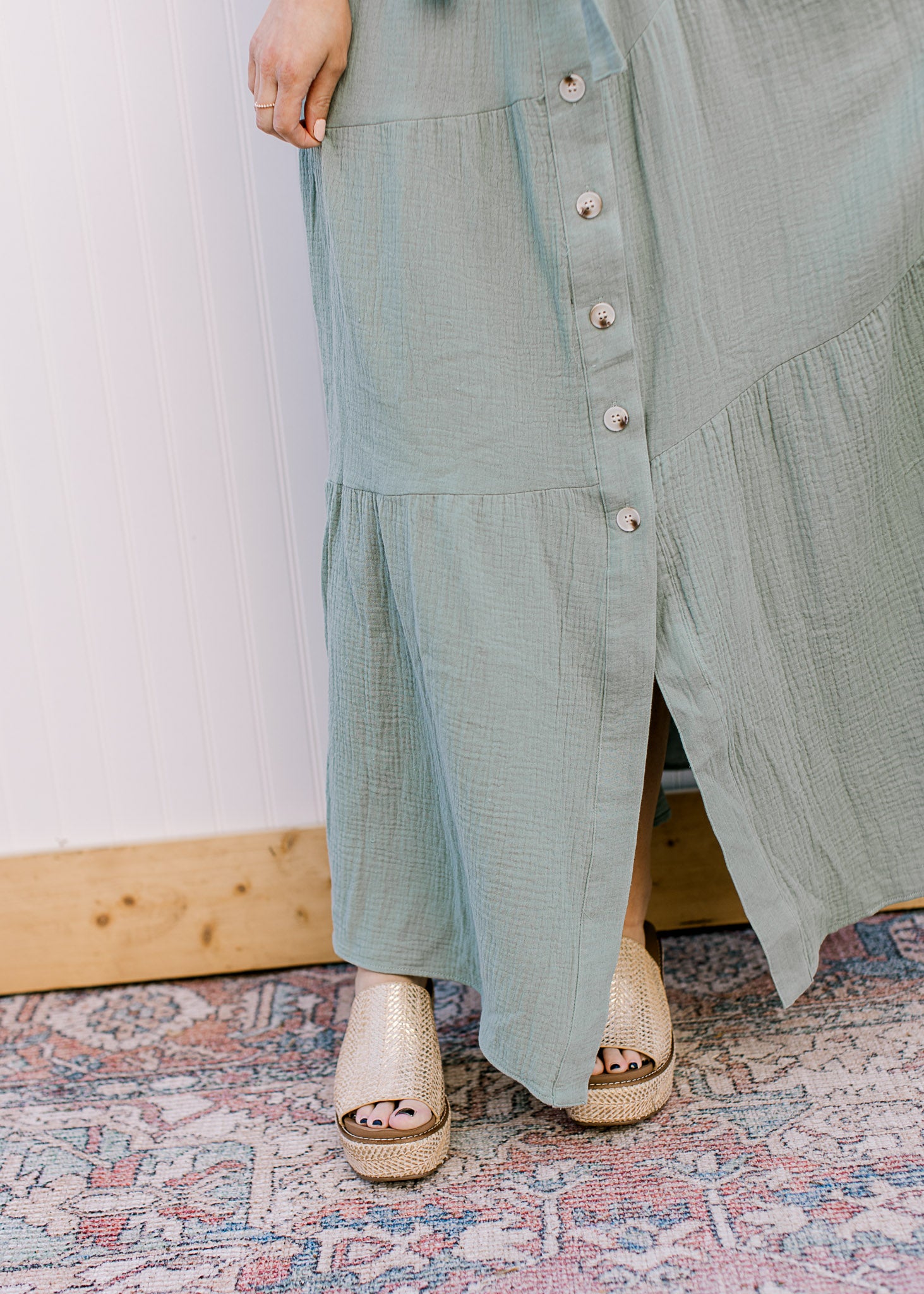 Close up of tiers along the skirt of a sage green maxi with button front and short sleeves. 