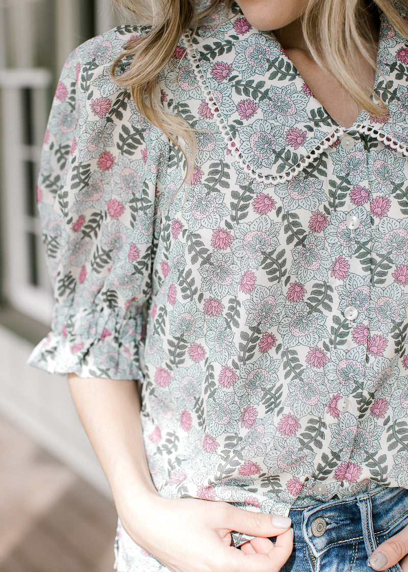 Model wearing a cream top with sage and pink floral and exaggerated collar with lace scallop trim.