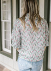 Back view of Model wearing a cream top with sage and pink floral and short sleeves with ruffles.