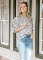 Model wearing jeans and a cream top with floral, short sleeves and an exaggerated collar. 