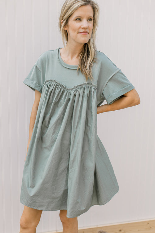 Model wearing a sage dress with pockets, contrasting material, short sleeves and ruffle detail. 