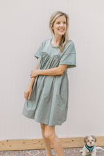 Model wearing a sage above the knee dress with contrasting material, short sleeves and pockets.