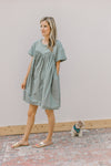 Model wearing sandals and a sage above the knee dress with contrasting material and short sleeves