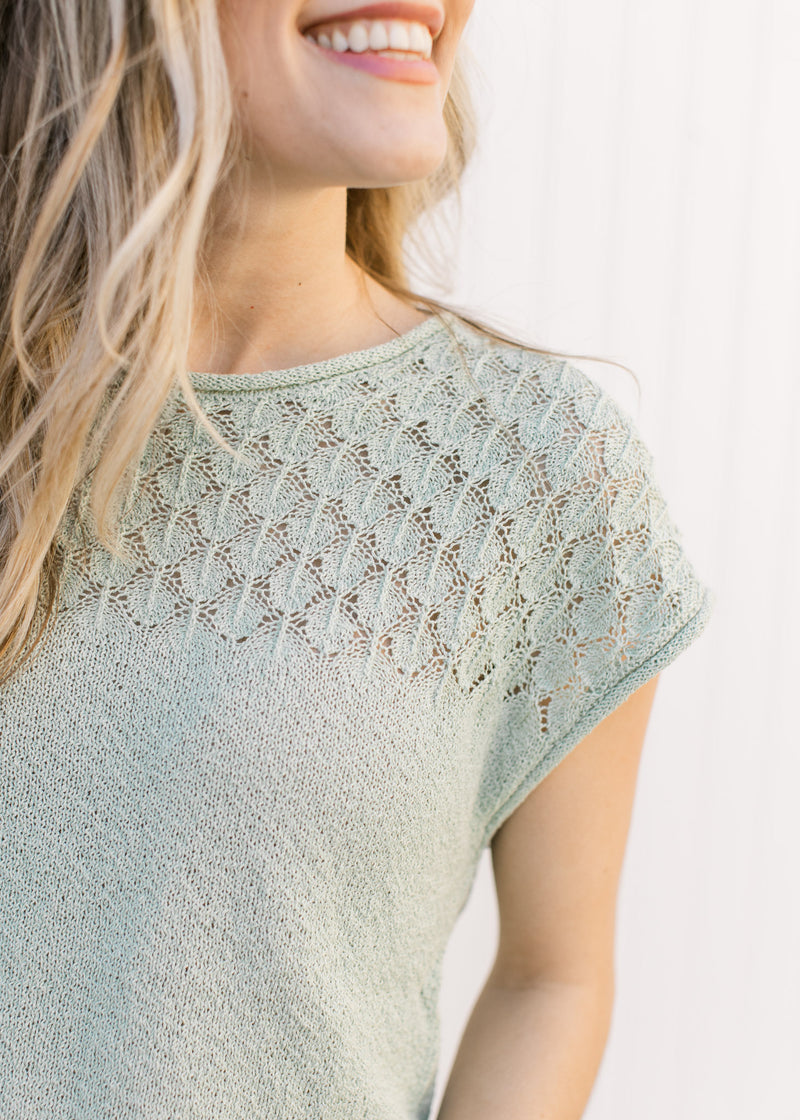 Close up of knit detailing on the bodice of a sage sweater with a round neck and capped sleeves.