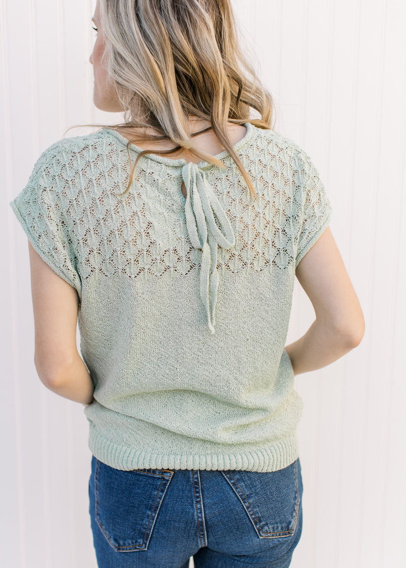 Back view of Model wearing a sage short sleeve sweater with knit detaili and back tie closure. 