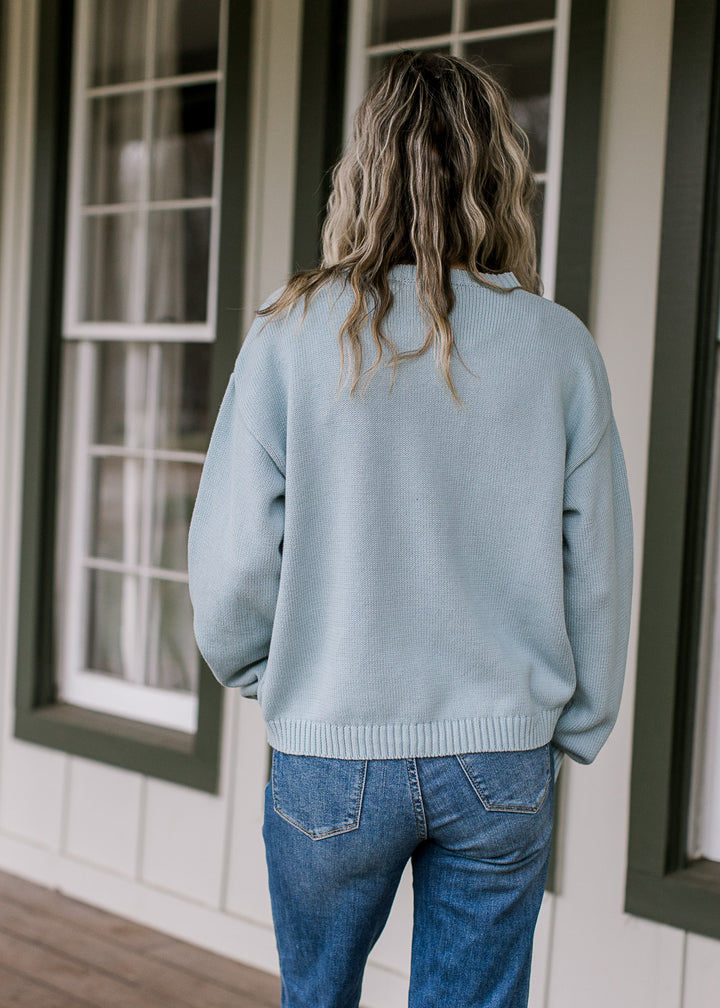 Back view of Model wearing a light blue sweater with a long sleeves and a round neck. 