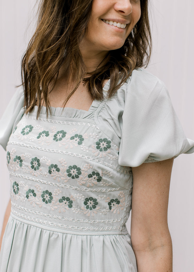 Close up of embroidered detail on a soft sage dress with a square neck and bubble short sleeves. 
