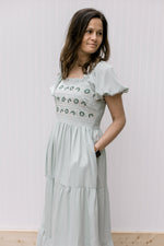 Model wearing a soft sage midi with a embroidered bodice, square neck and pockets.