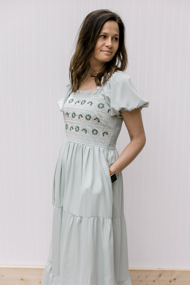Model wearing a soft sage midi with a embroidered bodice, square neck and pockets.