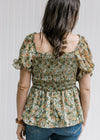 Back view of Model wearing a sage top with a floral pattern, smocked bodice and bubble short sleeves