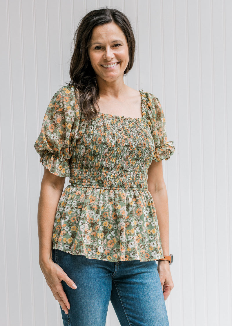 Model wearing jeans with a sage square neck top with orange, pink and blue floral and short sleeves.