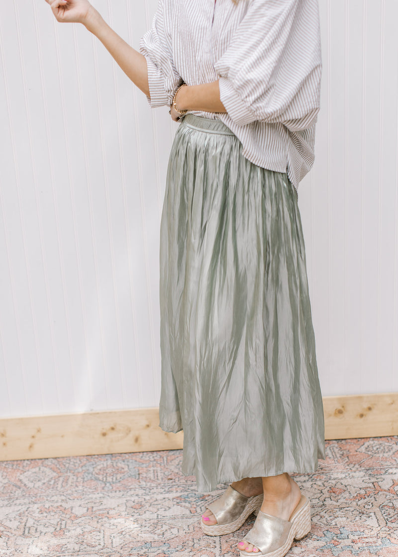 Model wearing a sage maxi skirt with an elastic waist band and comprised of polyester. 