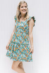 Model wearing a sage above the knee dress with an orange, blue and purple floral pattern. 