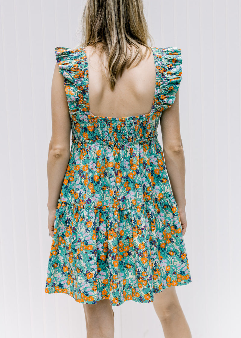 Back view of a model wearing a tiered sage floral dress with a square back and ruffle sleeves.