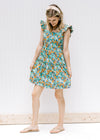 Model wearing a tiered sage floral dress with a square back and ruffle sleeves and sandals. 