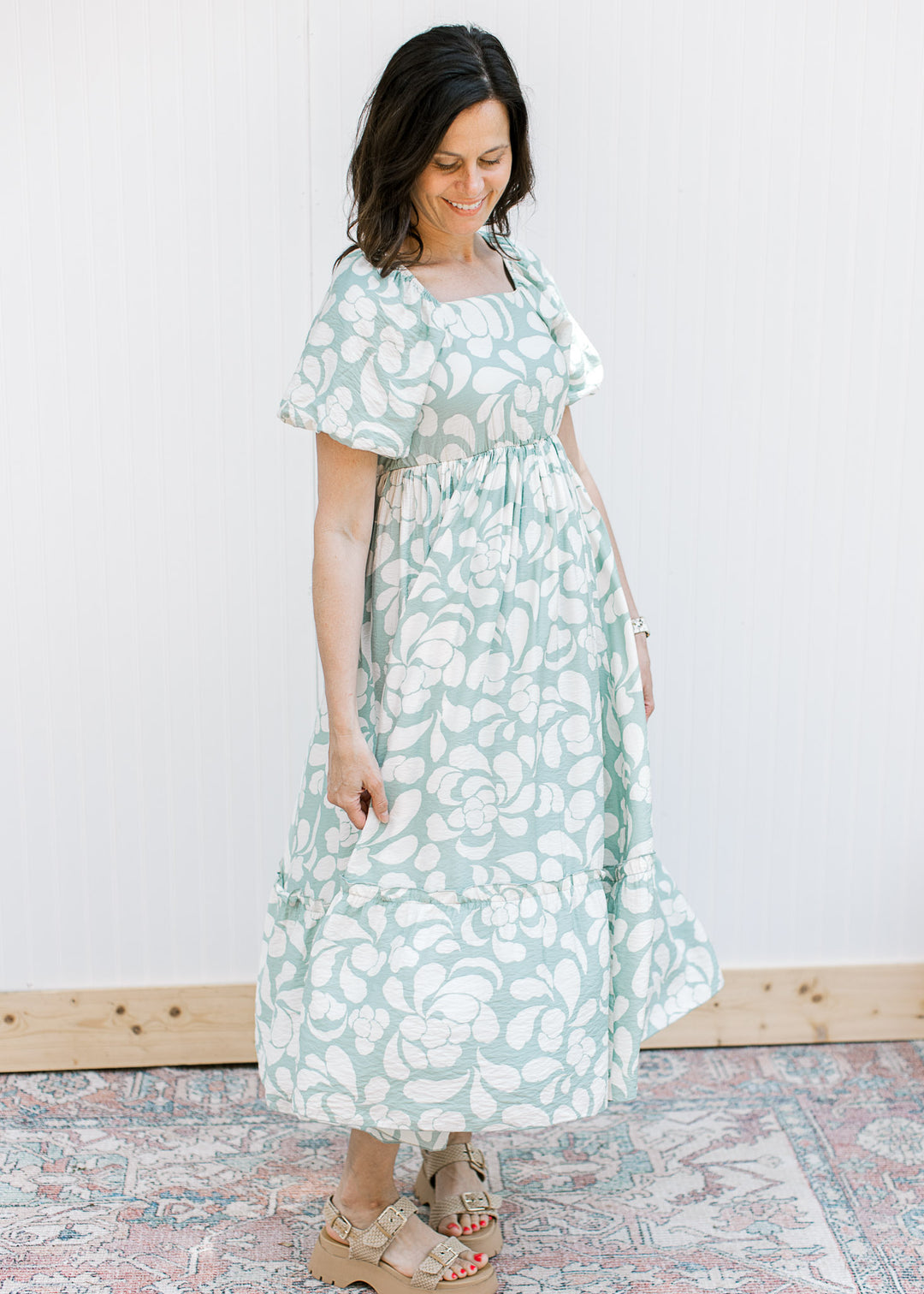 Model wearing a sage midi with a cream pattern, short bubble sleeves and square neck with elastic.