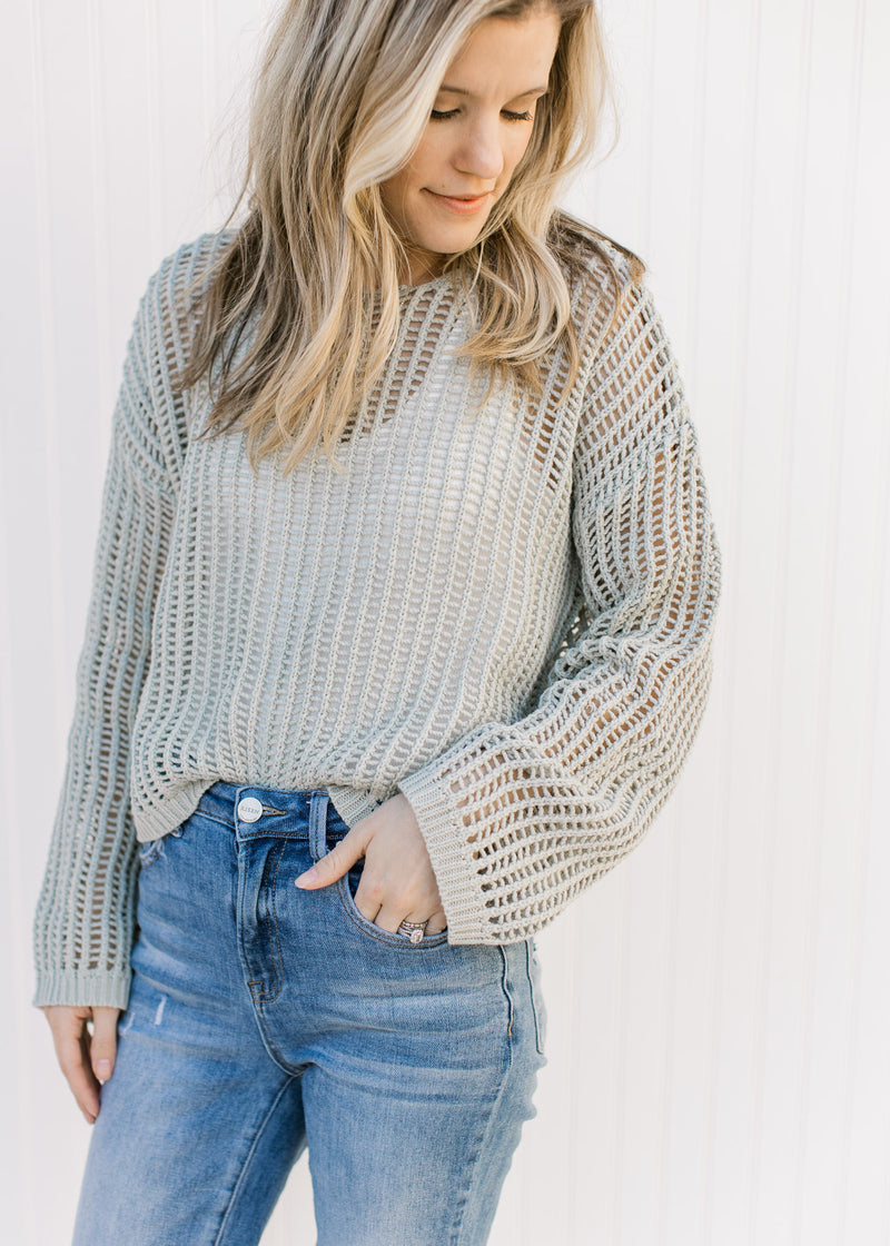 Model wearing a sage open weave sweater with long sleeves and a round neck. 