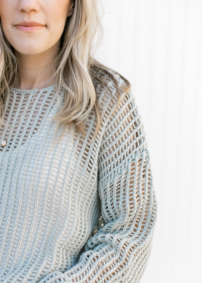 Close up of open weave on a open weave sage sweater with long sleeves and a round neckline.