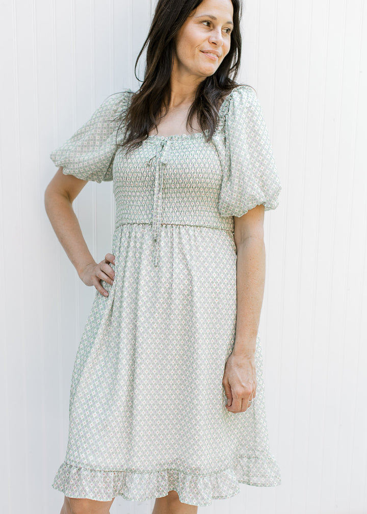 Model wearing a sage knee length dress with cream pattern smocked bust and  square neck.