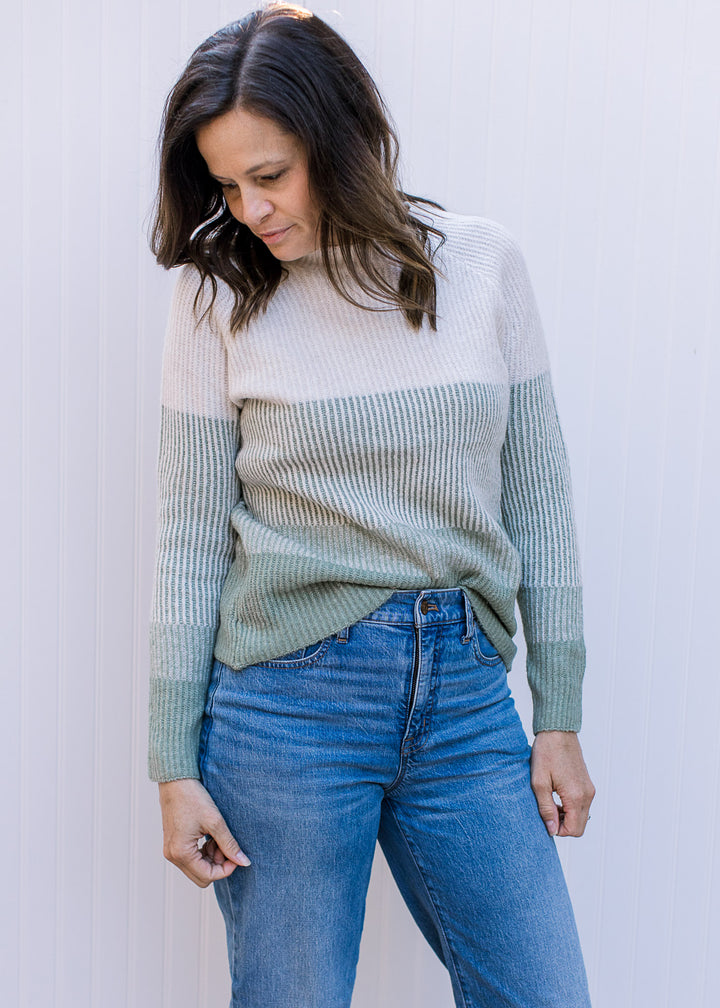 Model wearing jeans with a cream and sage ribbed sweater with long sleeves and a round neck.