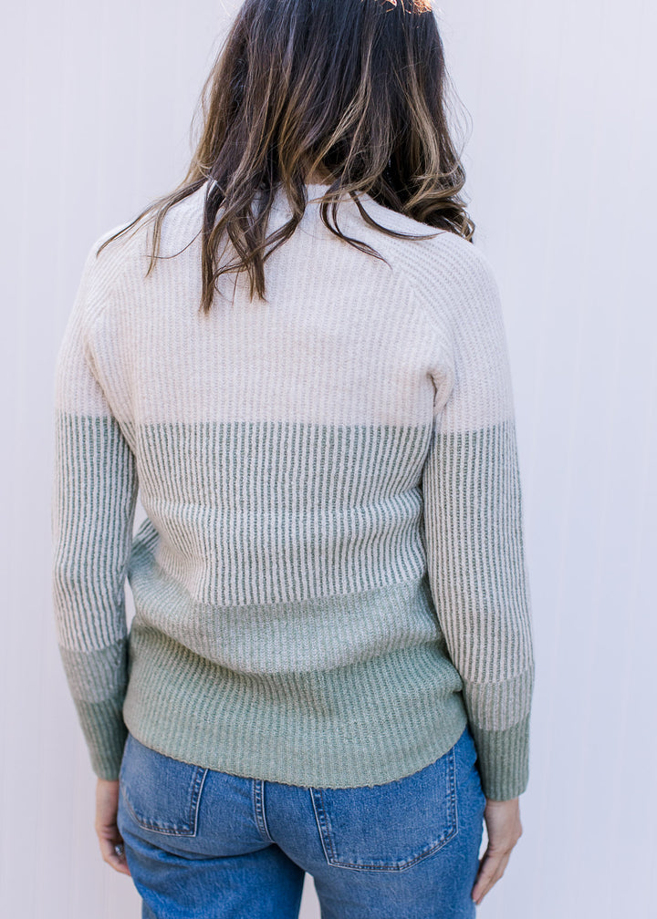 Back view of Model wearing a cream and sage ribbed sweater with long sleeves and a round neck.