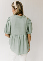 Back view of Model wearing a sage colored babydoll top with tone on tone stripes and short sleeves. 