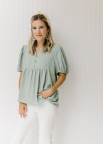 Model wearing a sage colored top with tone on tone stripes, bubble short sleeves and a hi-low hem.