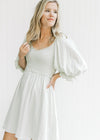 Model wearing a pale sage above the knee dress with a smocked bodice and 3/4 bubble sleeves. 