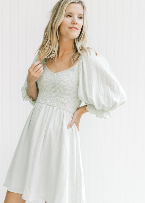 Model wearing a pale sage above the knee dress with a smocked bodice and 3/4 bubble sleeves. 