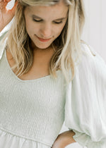 Close up of smocked bodice and 3/4 bubble sleeve on a model in a pale sage above the knee dress.