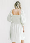 Back view of Model wearing a pale sage above the knee dress with a smocked bodice and bubble sleeves