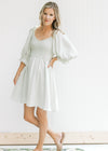 Model wearing sandals with a sage above the knee dress with a smocked bodice and bubble sleeves. 